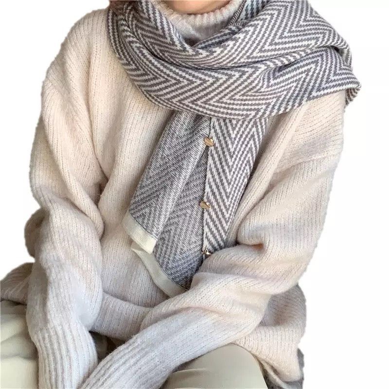 Cozy model wearing a beige oversized sweater paired with a stylish gray and white herringbone patterned scarf, showcasing a button detail for added charm and warmth.