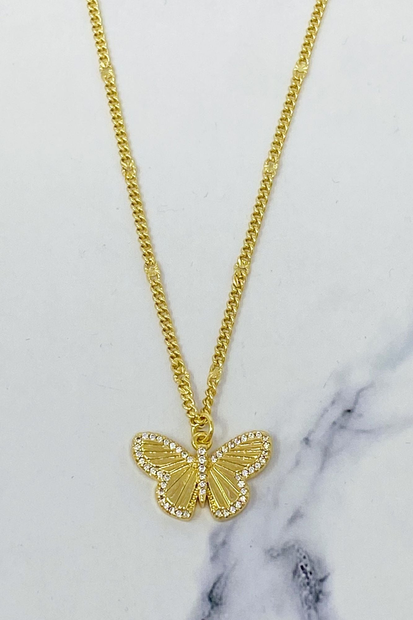 Gold butterfly pendant necklace with sparkling rhinestones on a dainty chain, set against a marble background.