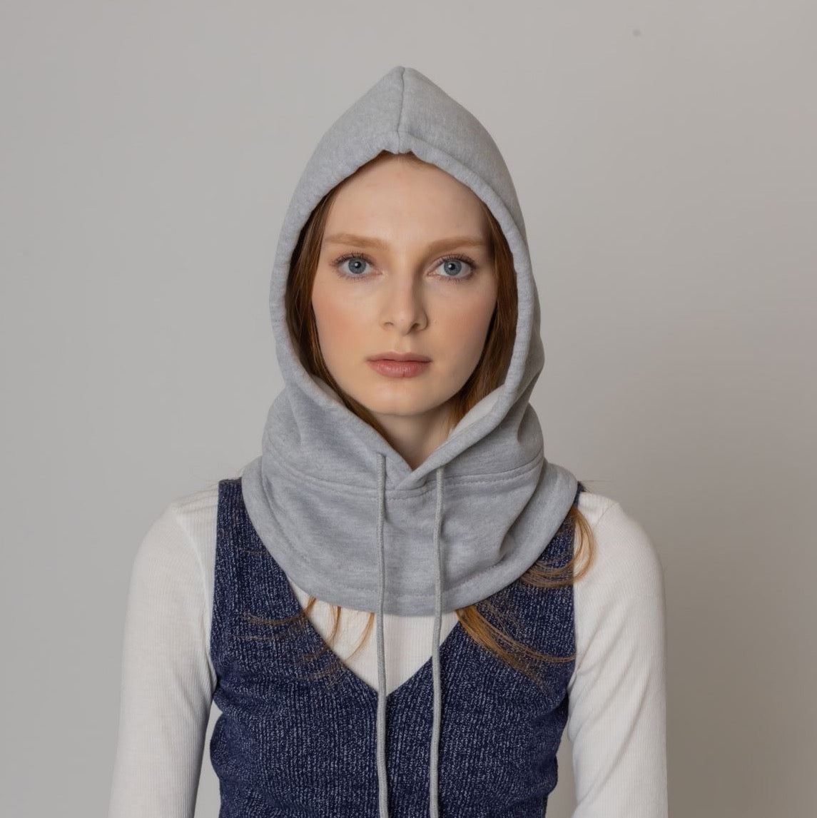 Gray hoodie with a cowl neck design, paired with a dark blue textured vest over a white long-sleeve top, showcasing a fashionable and cozy winter look.