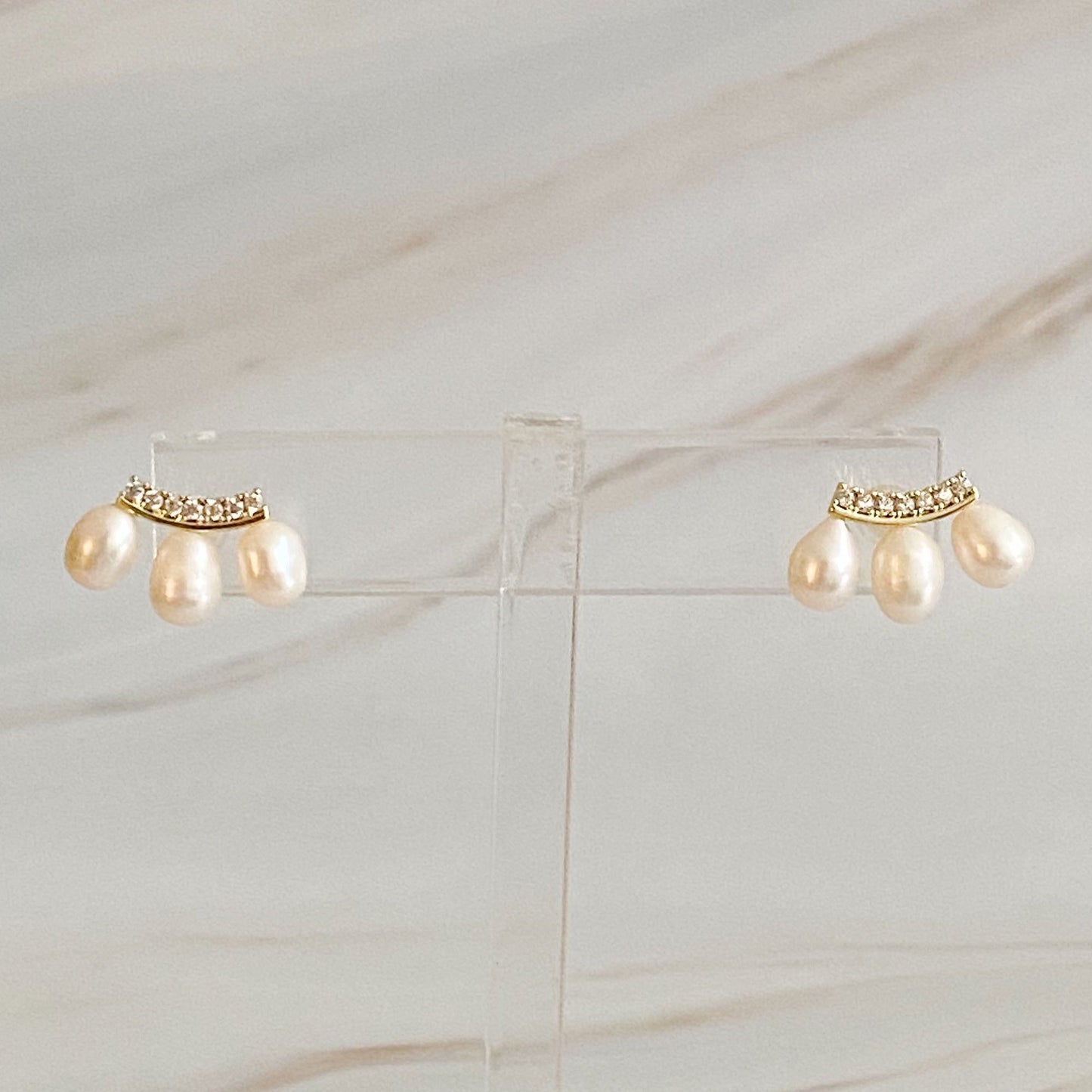 Elegant pearl drop earrings with sparkling crystal accents, set against a light marble background.