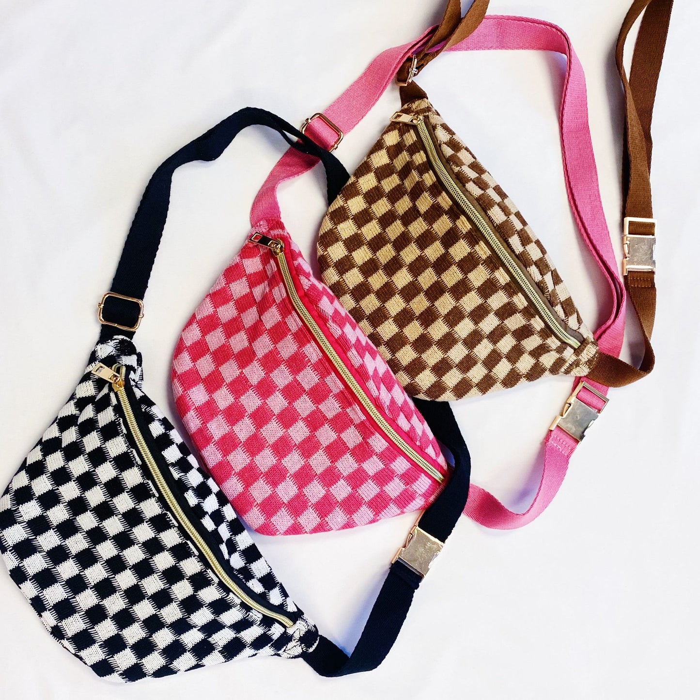 Three stylish checkered crossbody bags in pink, black, and brown with gold zippers, displayed on a white background.