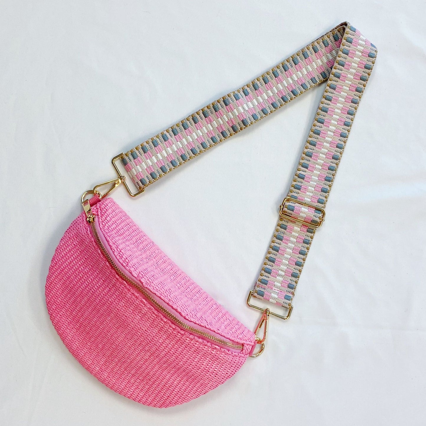 Stylish pink crescent-shaped crossbody bag with a colorful woven strap and gold zipper detailing, ideal for trendy outings and casual wear.