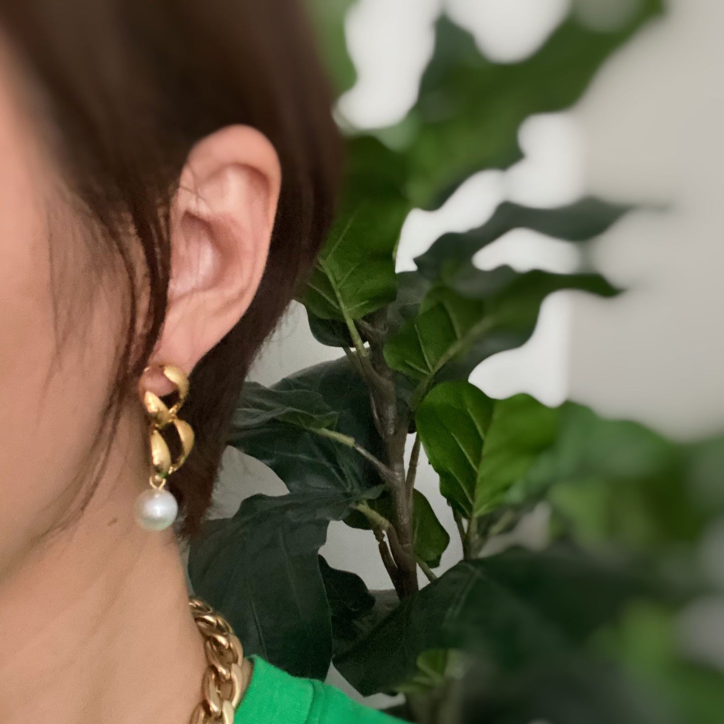 Elegant gold earrings with twisting design and pearl accent, worn by a woman against a backdrop of green foliage.