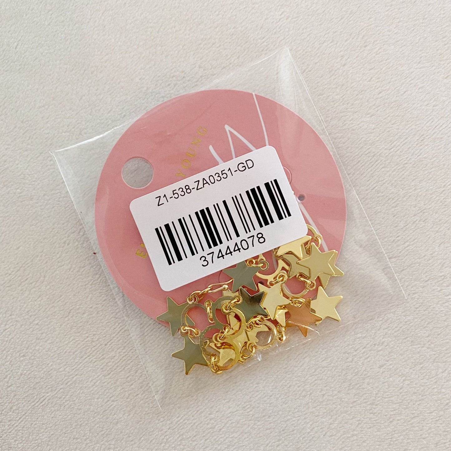 Gold star-shaped charms packaged in a clear plastic bag with a pink circular label, ideal for jewelry making and craft projects.