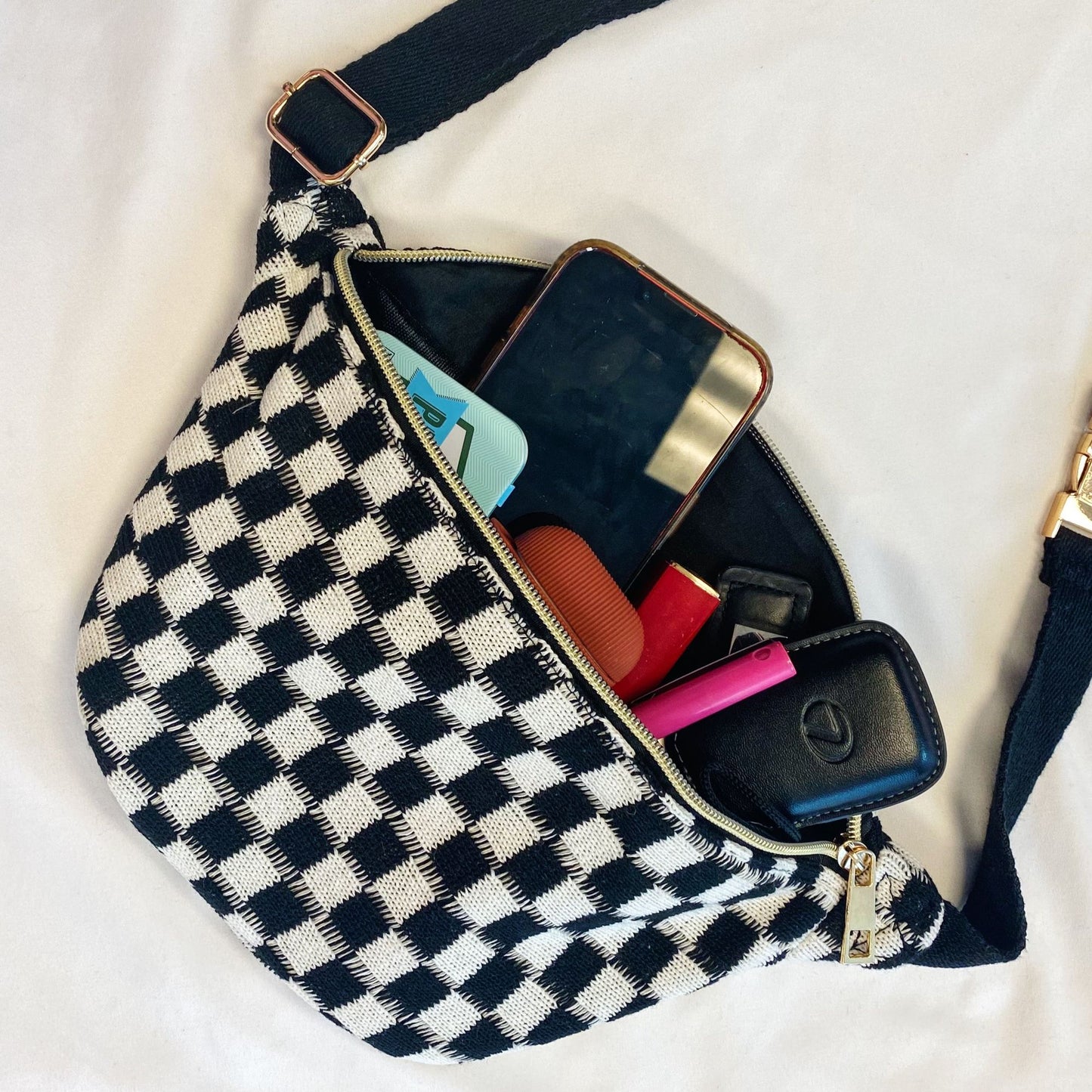 Stylish black and white checkered handbag with a zippered closure, partially open to reveal a smartphone, wallet, and various small items inside.