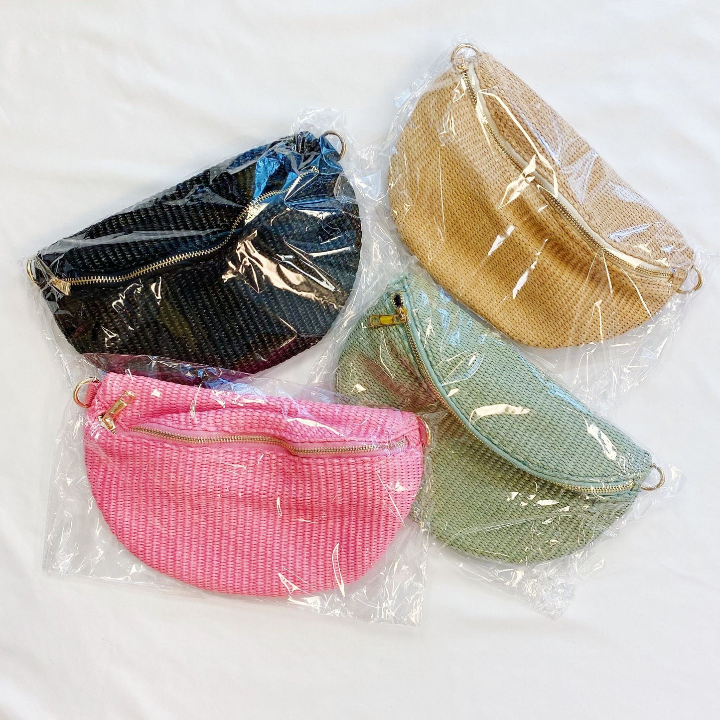 Variety of four stylish half-moon shaped woven bags in black, beige, green, and pink, each in clear packaging, displayed on a white background.