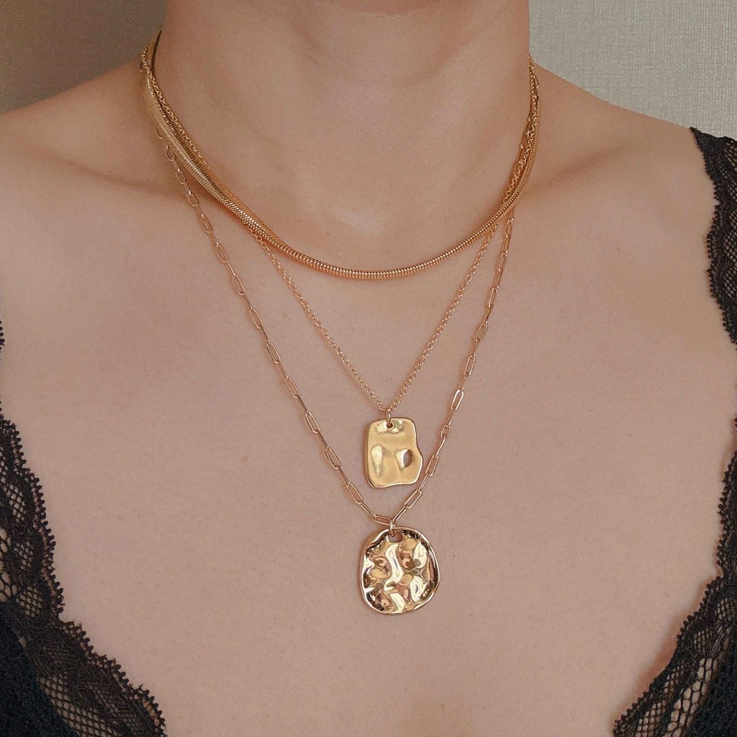 Layered gold necklaces featuring delicate chains and unique pendants, styled on a model wearing a lace top.