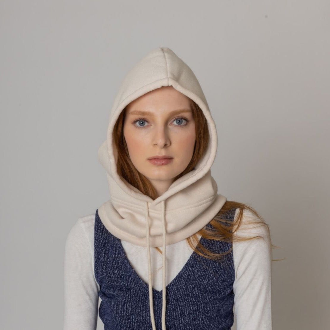 Woman wearing a cream-colored hooded sweatshirt layered over a navy blue sweater, showcasing a trendy casual style against a neutral background.