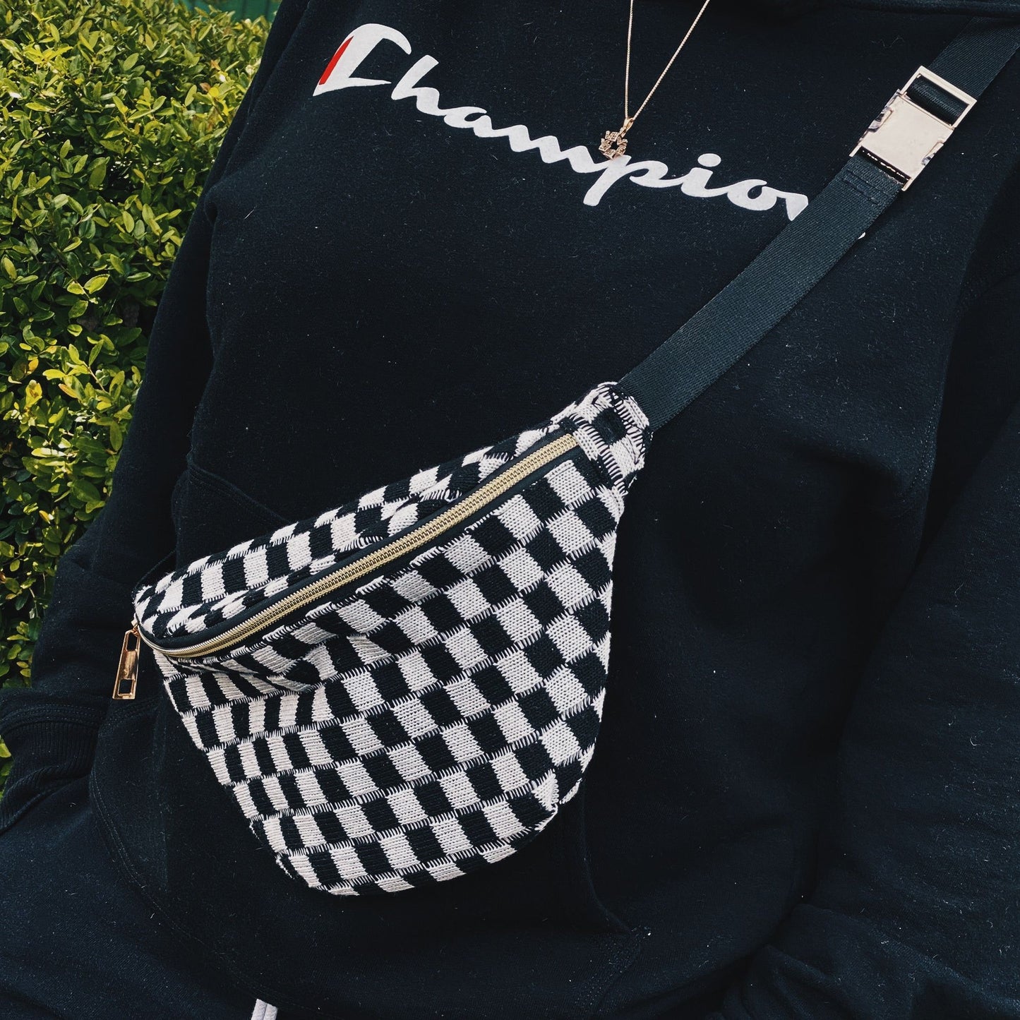 Fashionable black and white checkered fanny pack worn across the chest of a person in a black sweatshirt, showcasing its stylish design and adjustable strap.
