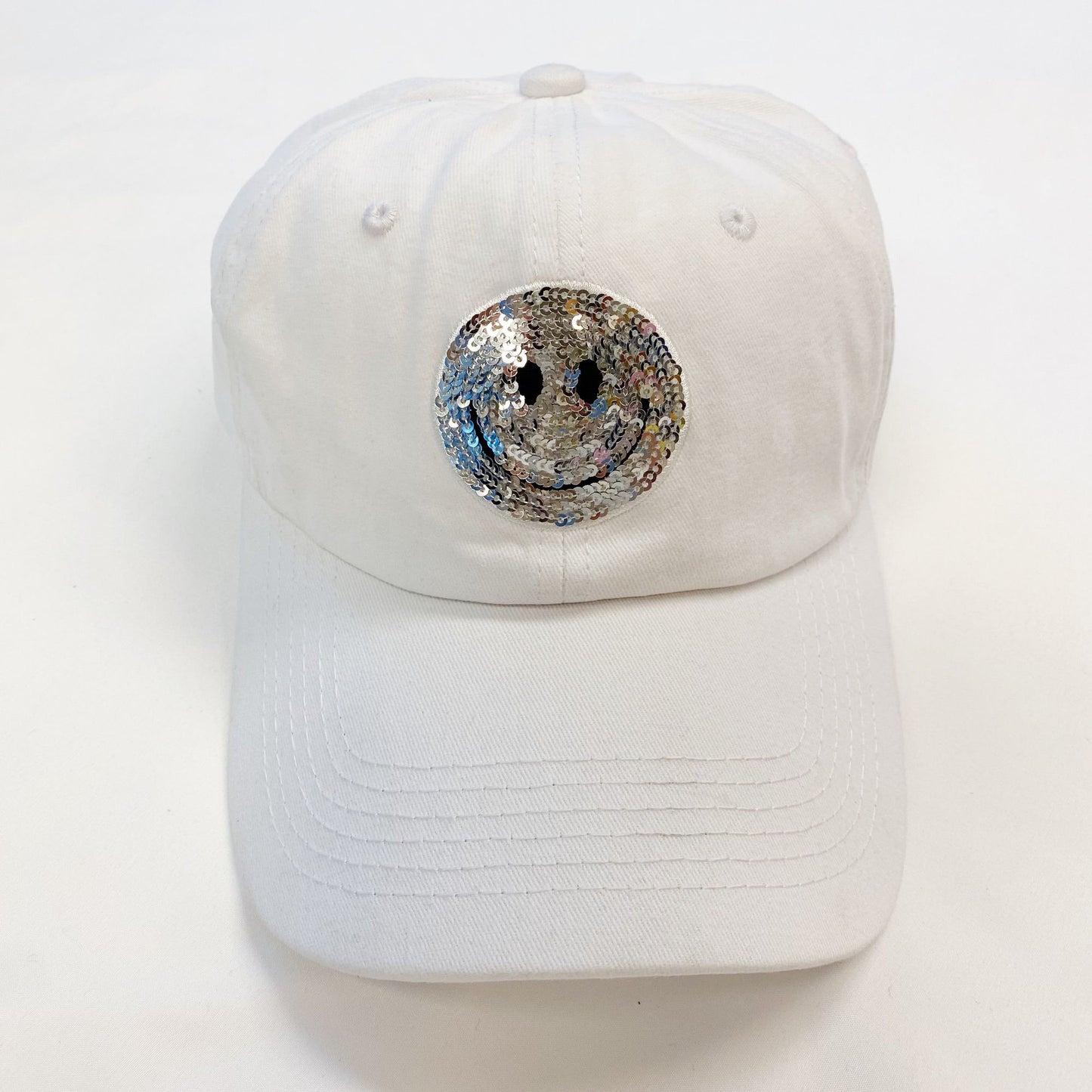 White baseball cap featuring a sparkly silver smiley face sequin design on the front, perfect for casual wear and adding a fun touch to any outfit.