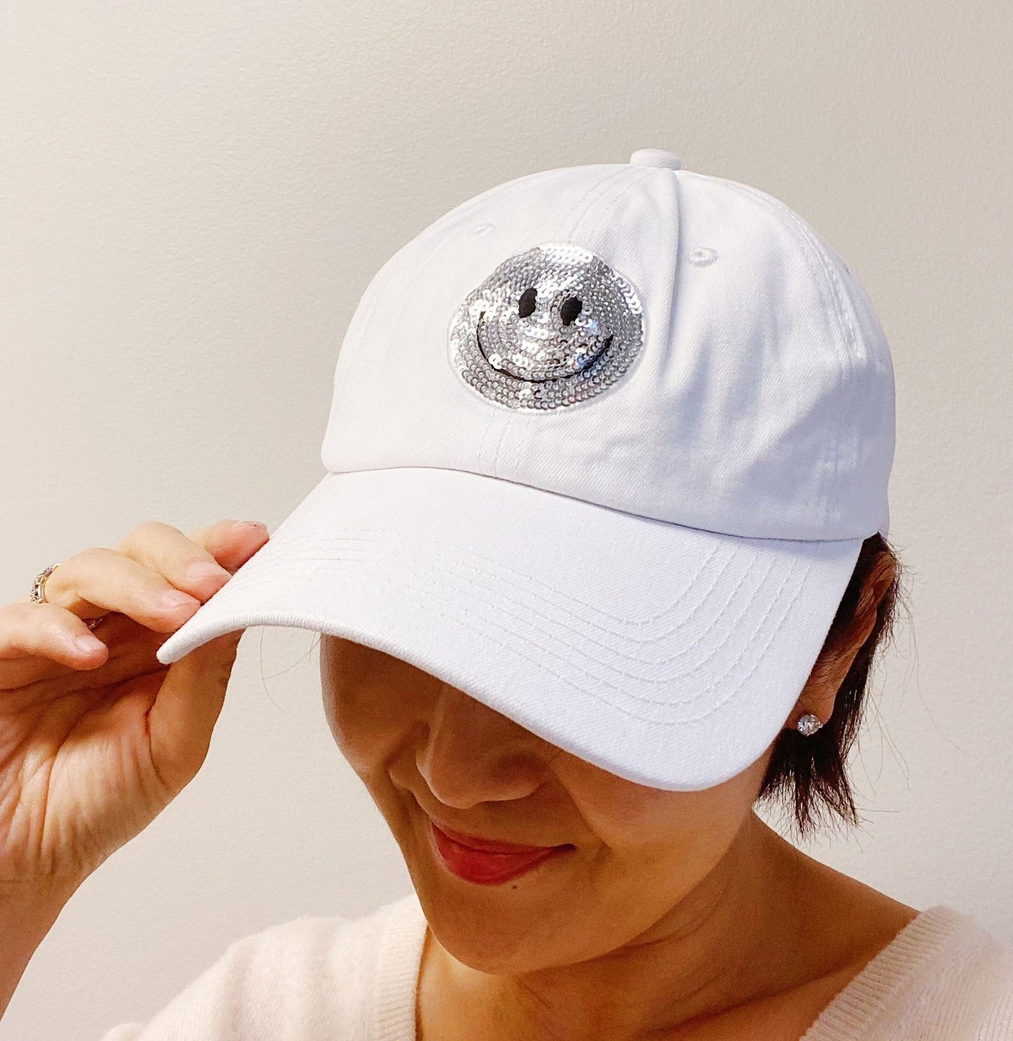 White baseball cap adorned with a sparkling silver smiley face patch, perfect for adding a playful touch to any outfit.