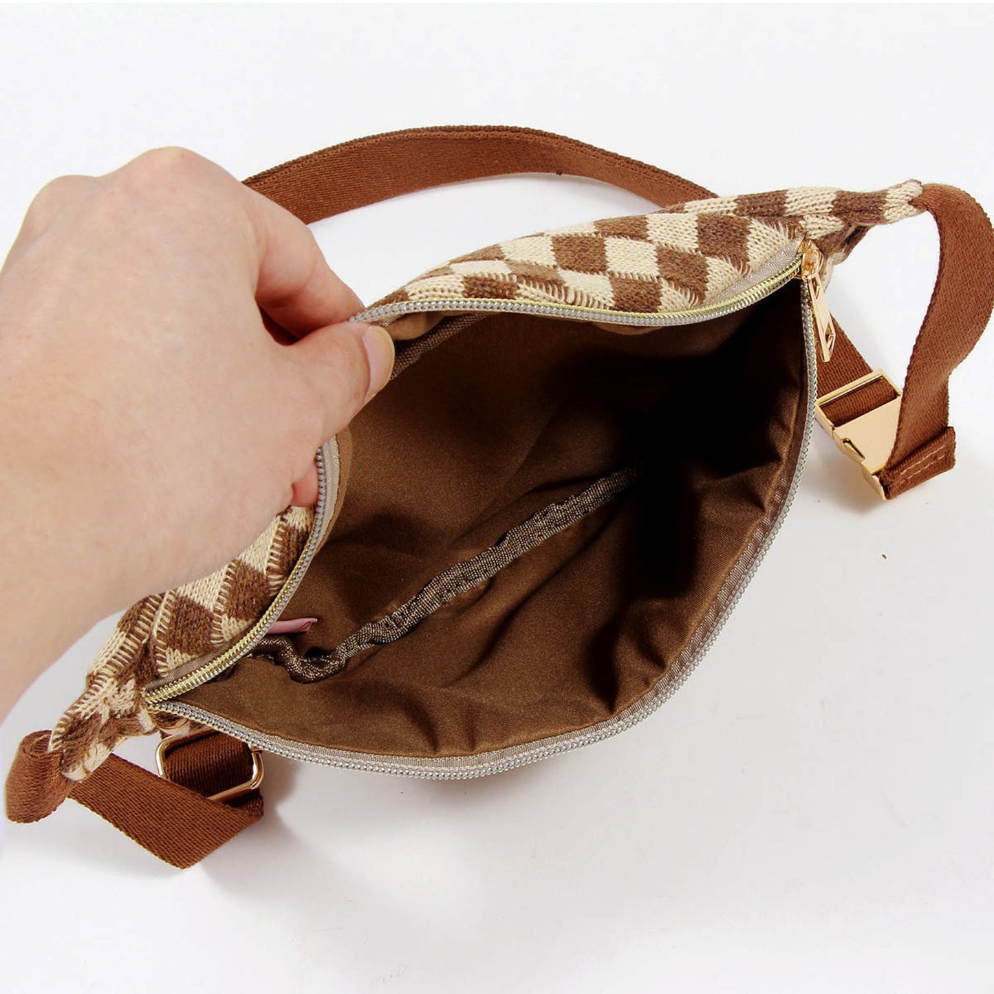 Hand revealing the interior of a stylish brown and beige checkered pattern handbag, showcasing a spacious lining and zipper closure.