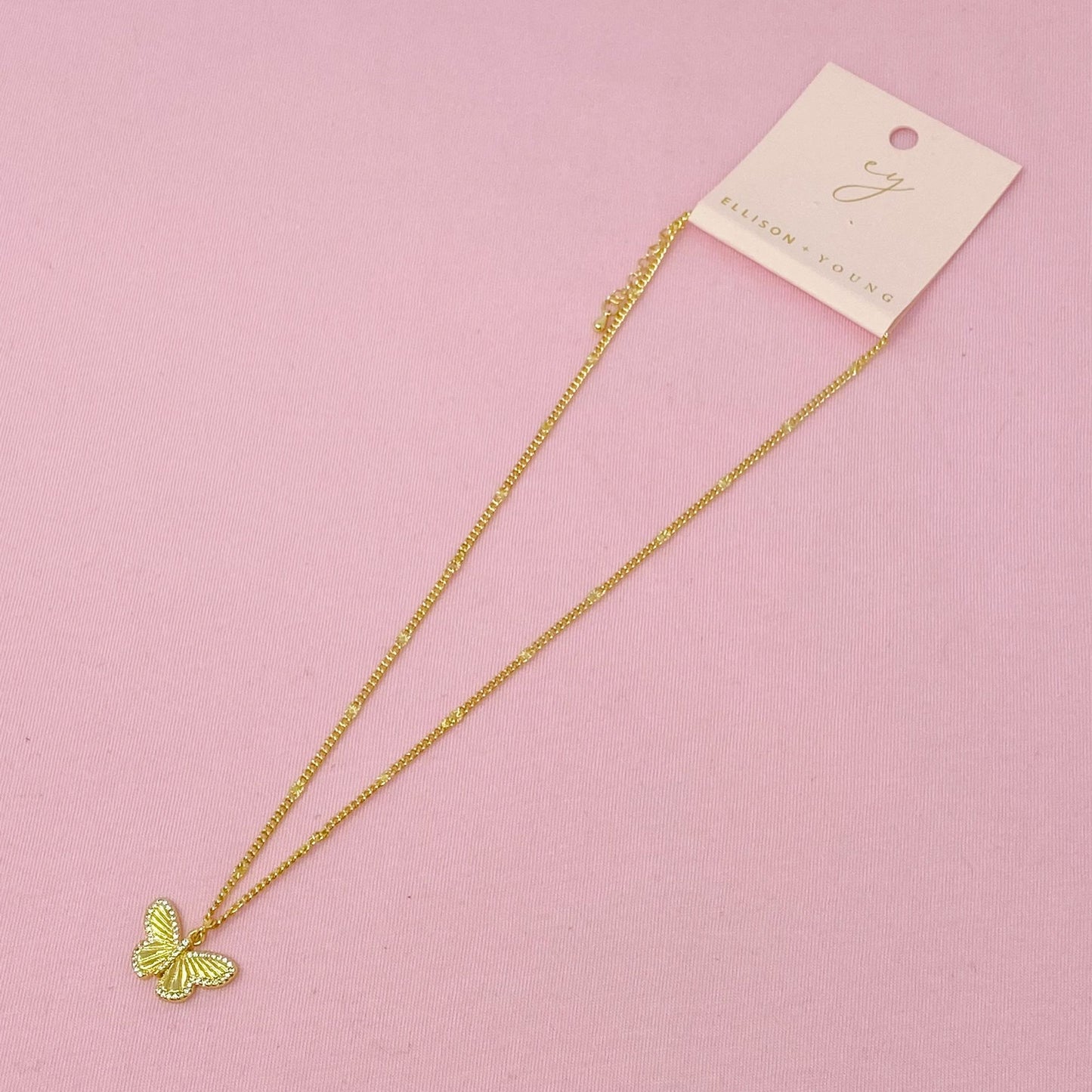 Gold butterfly pendant necklace on a delicate chain displayed on a pink background with a branded tag.