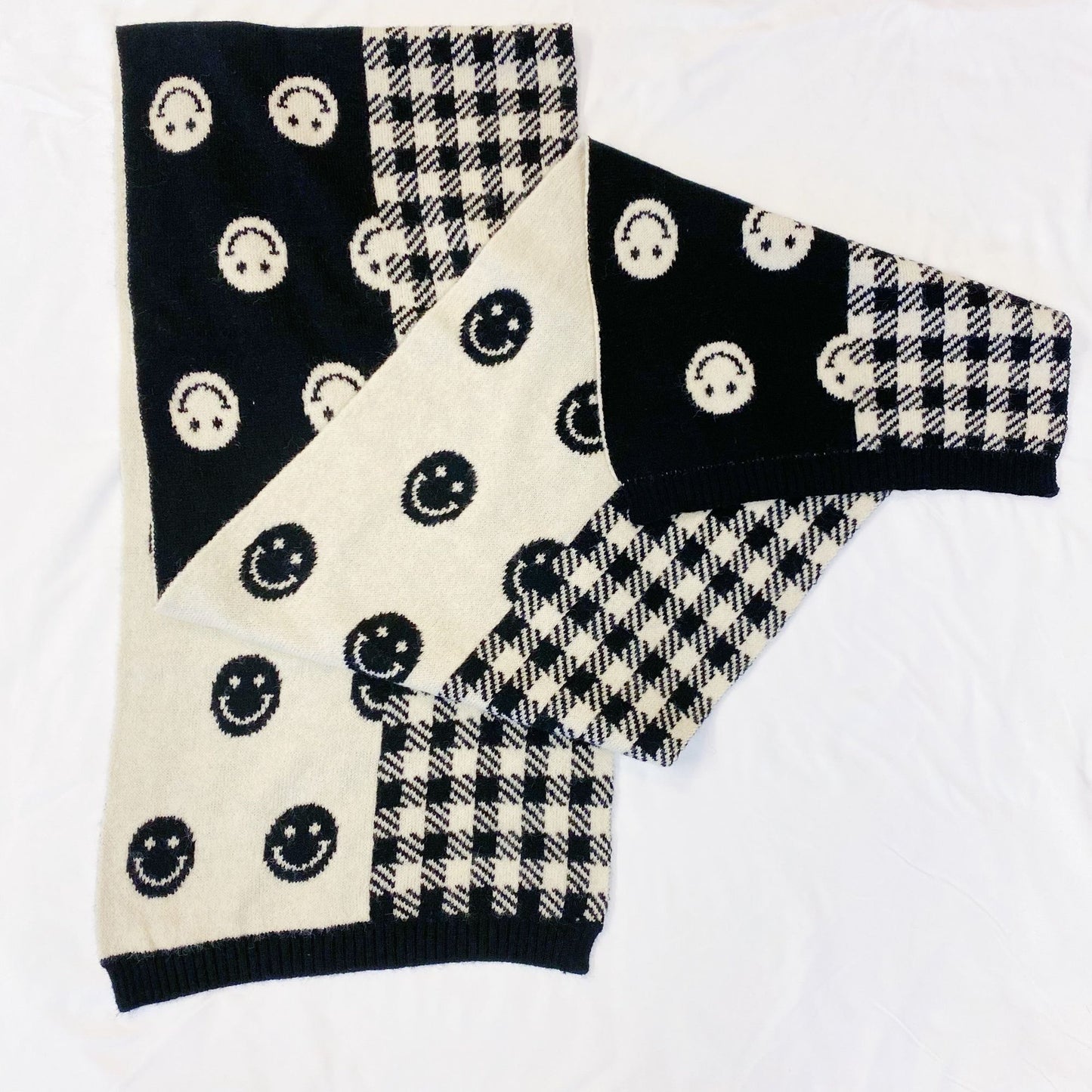 Stylish black and cream patterned scarf featuring smiley face motifs and a houndstooth design, perfect for adding a cozy and cheerful touch to any outfit.
