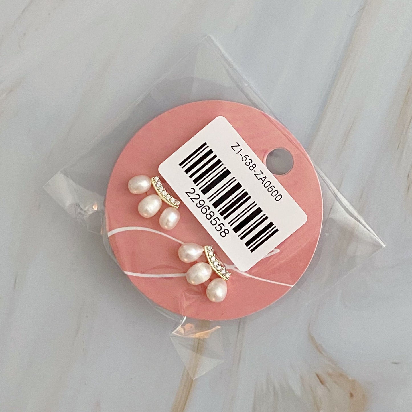 Elegant pearl stud earrings on a pink display card with a barcode, featuring a subtle design of golden bands and crystal accents.