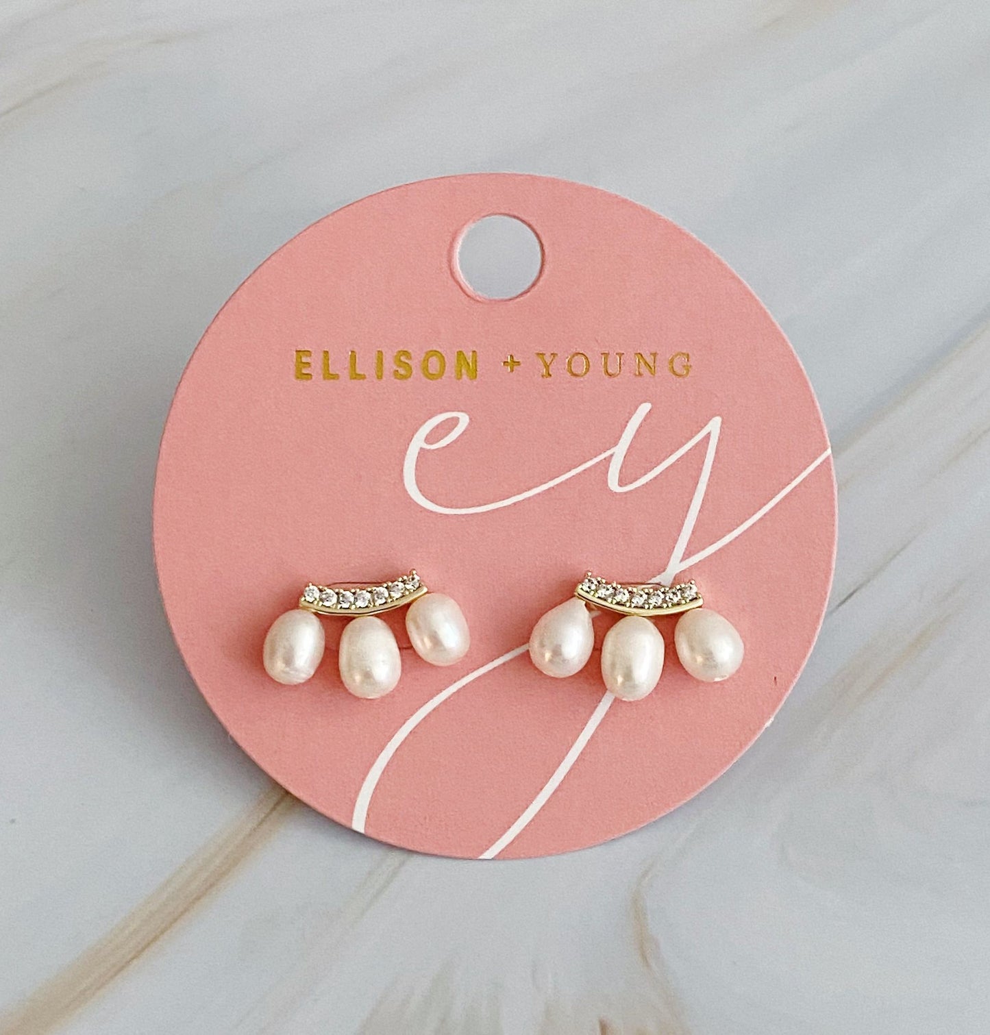 Pearl and rhinestone stud earrings displayed on a pink branded card by Ellison + Young.
