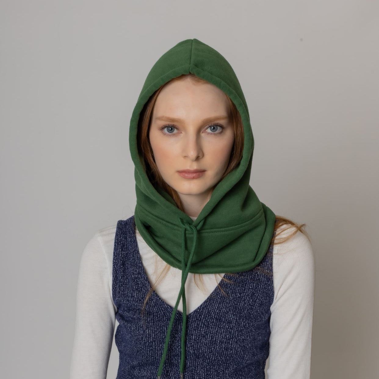 Model wearing a cozy green hooded sweatshirt, styled with a white long-sleeve top and a navy knit vest, against a neutral background.