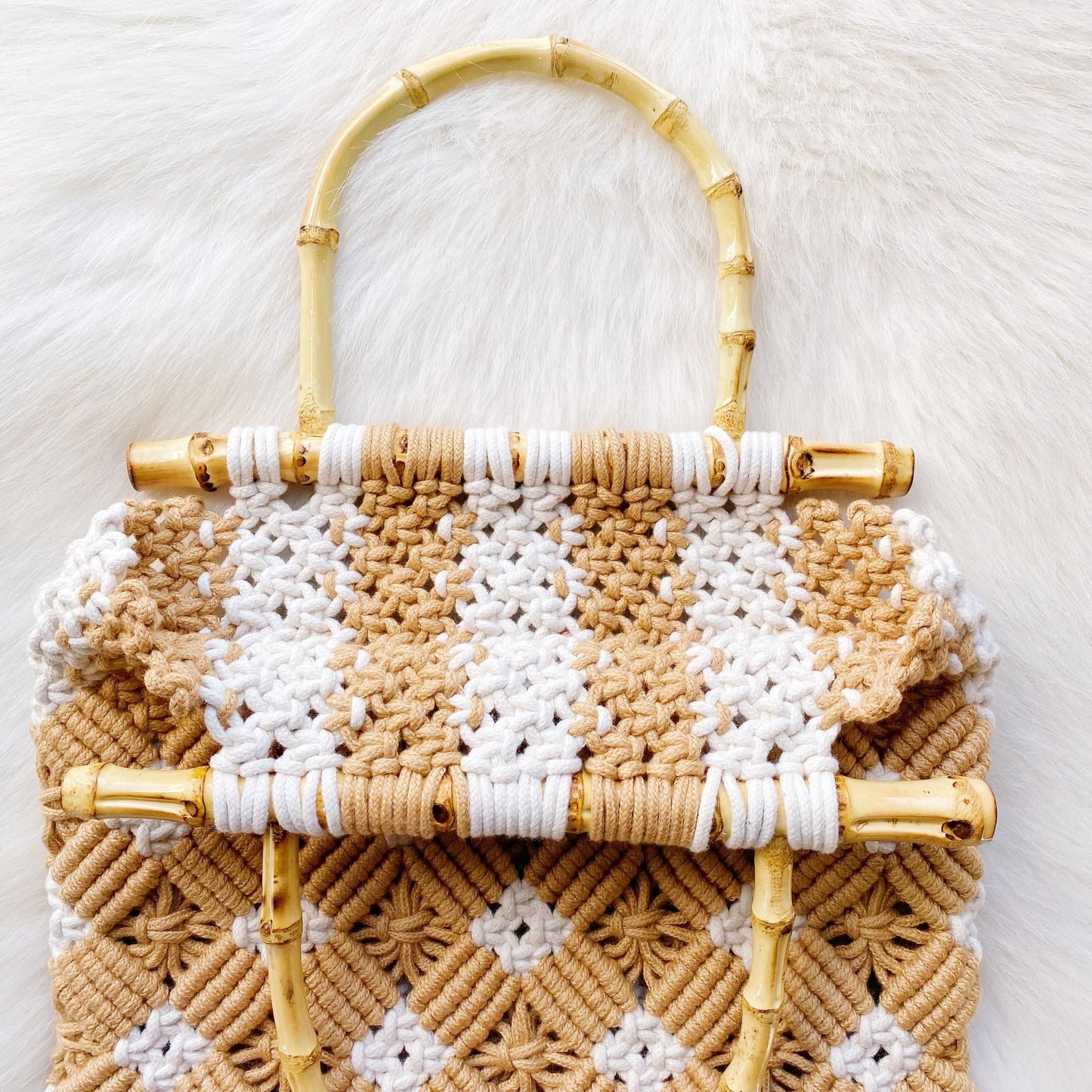 Handcrafted woven tote bag featuring a chic bamboo handle, with a stylish pattern in warm beige and white tones, set against a soft, textured background.