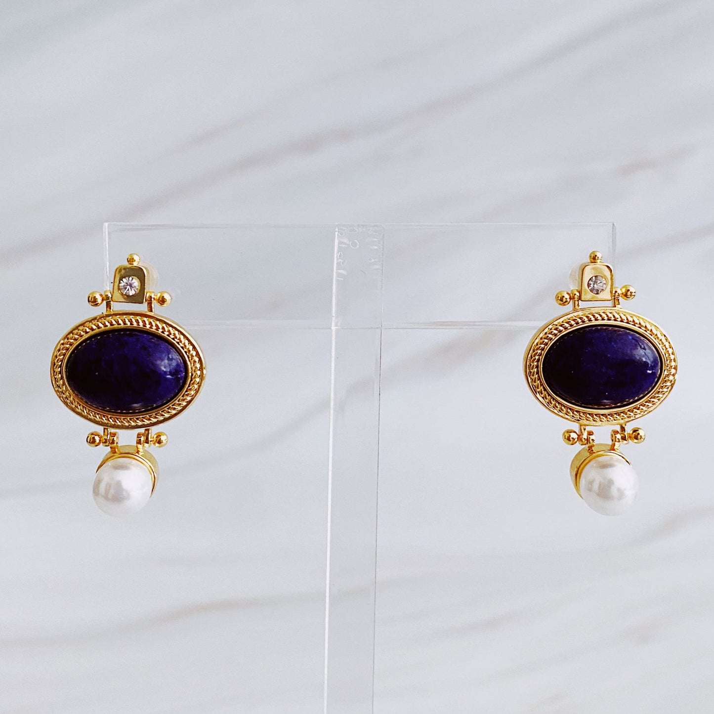 Elegant gold-tone earrings featuring deep blue lapis lazuli stones accompanied by a pearl drop, perfect for adding a touch of sophistication to any outfit.