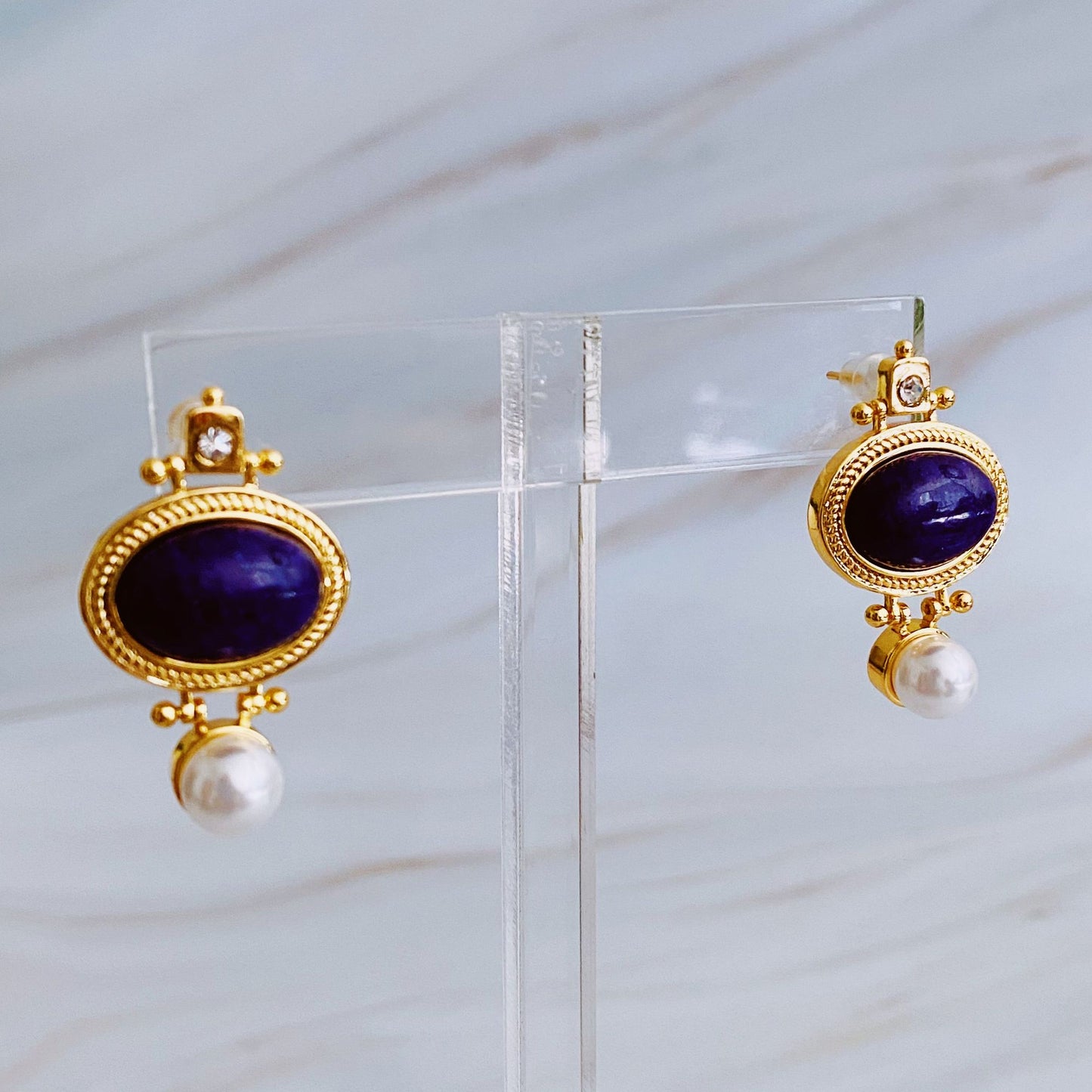 Elegant gold earrings featuring a deep blue lapis lazuli stone and a freshwater pearl drop, designed with intricate detailing and a sparkling crystal accent.