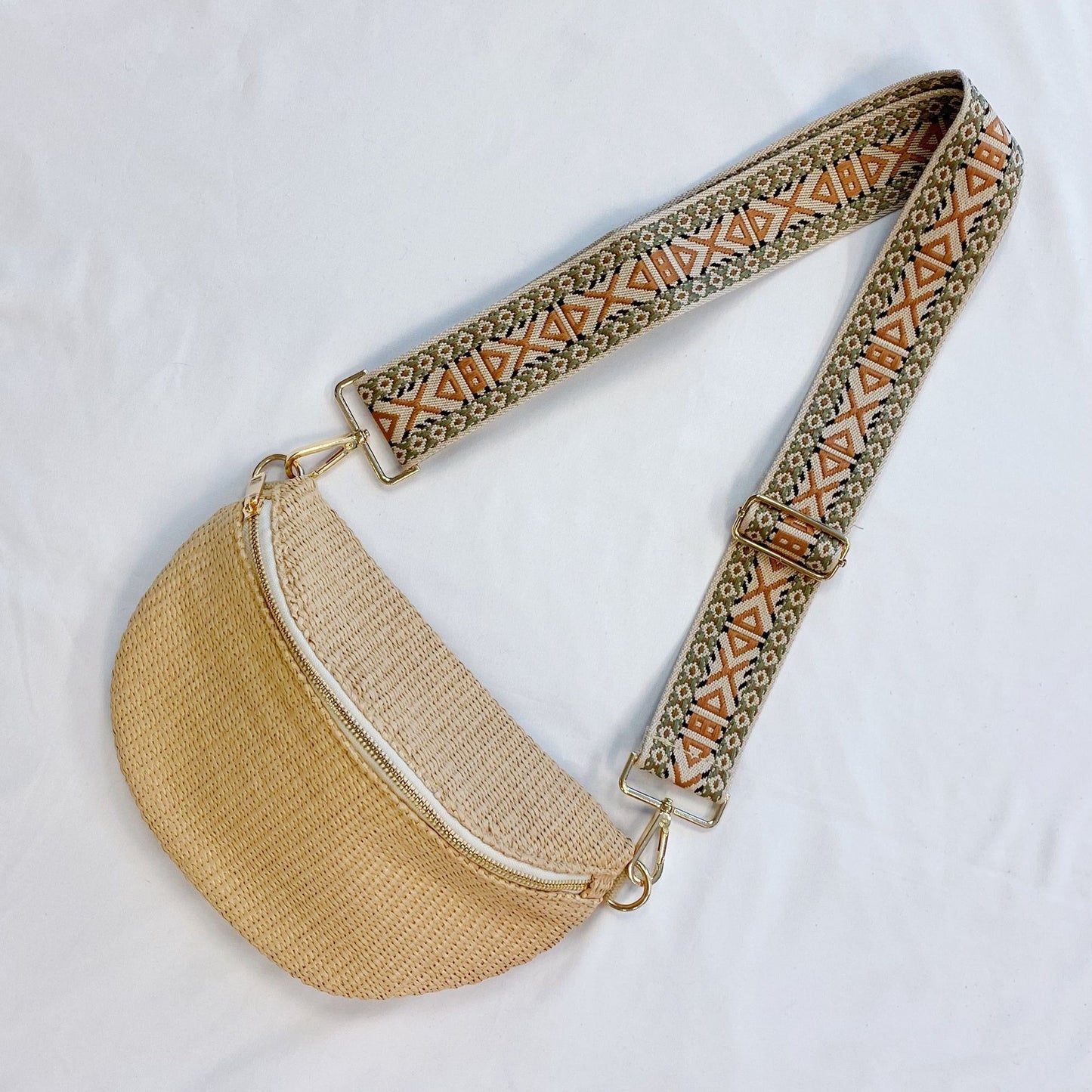 Stylish woven crossbody bag with a beige half-moon design, featuring a decorative patterned strap in earthy tones and gold hardware accents.
