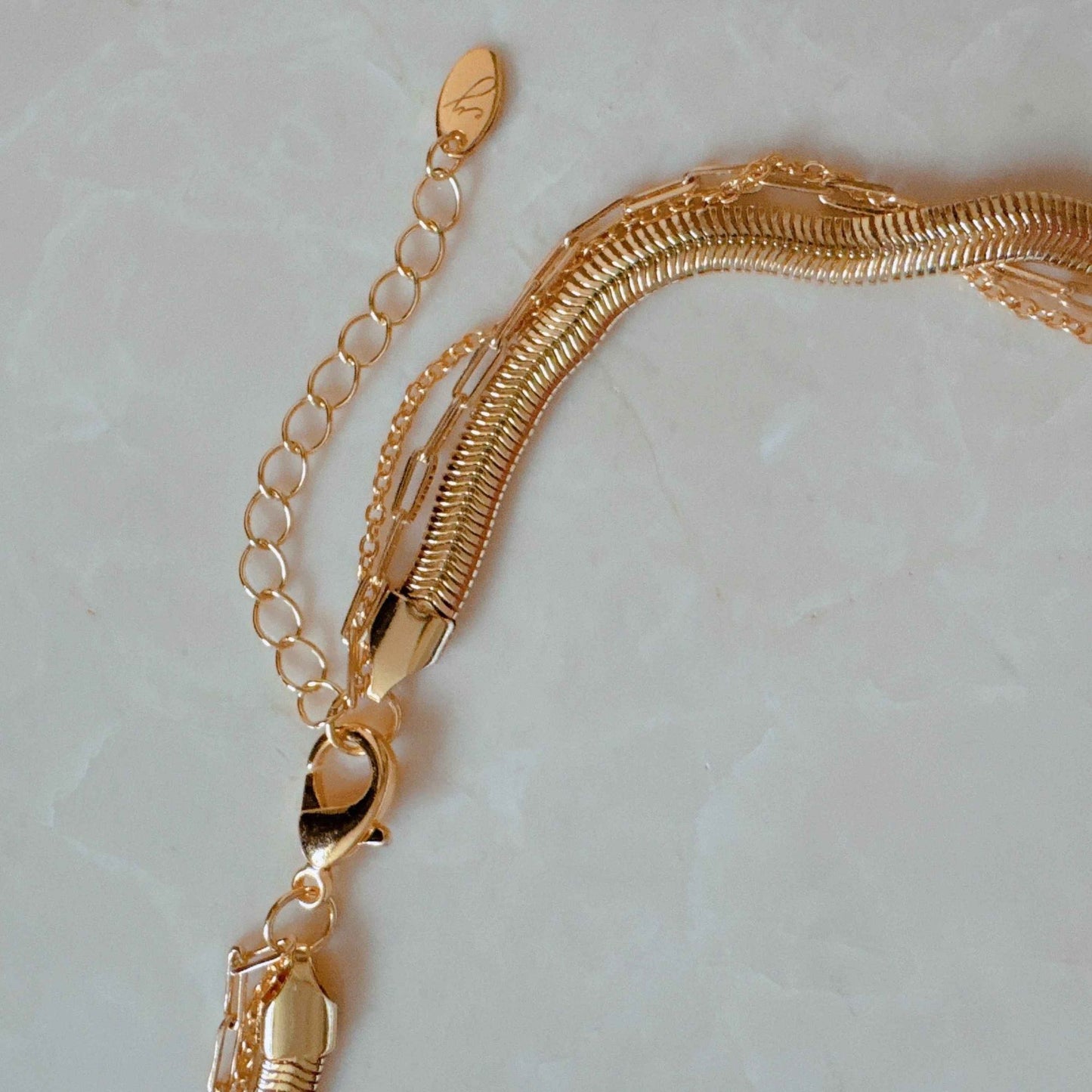 Close-up of a stylish gold chain necklace featuring a sleek snake chain with a secure lobster clasp and adjustable extension chain, set against a light marble background.