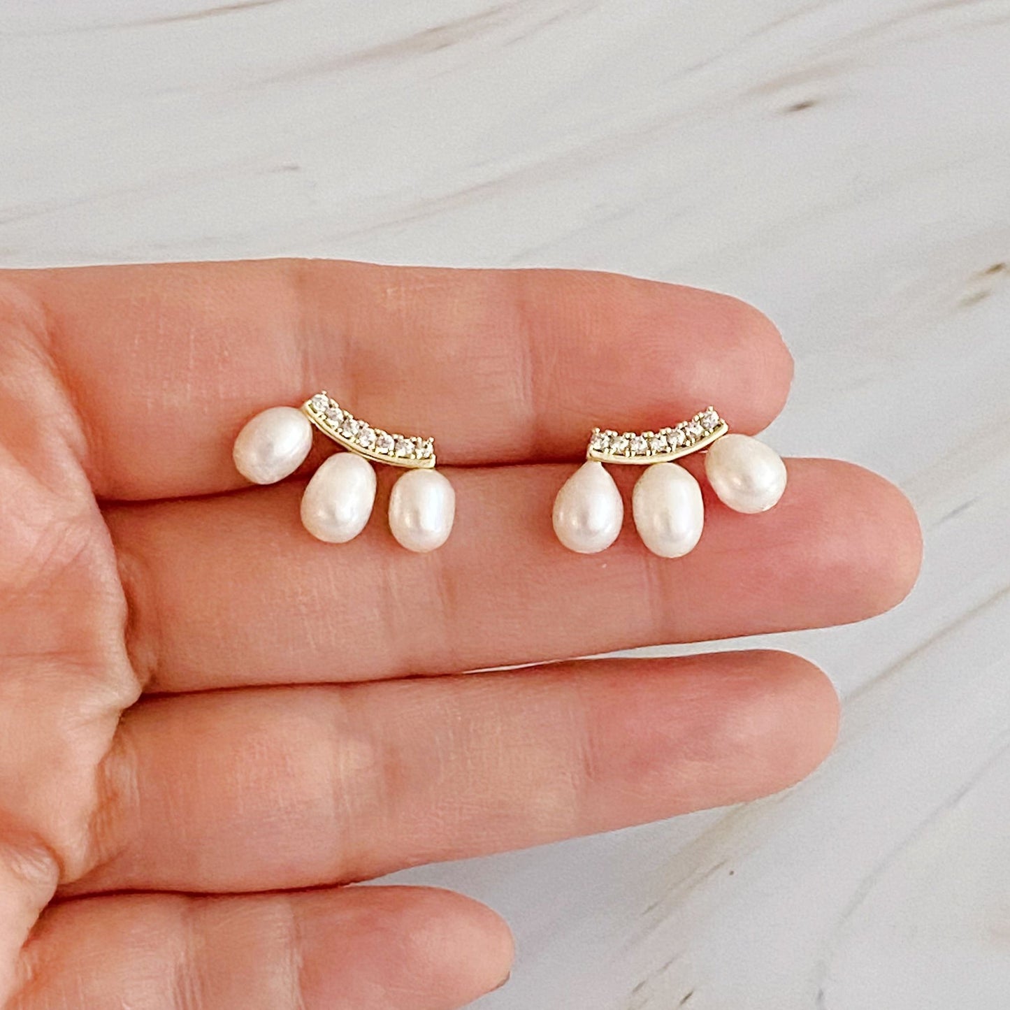 Elegant pearl and crystal earrings showcased on a hand, featuring four lustrous white pearls and a delicate gold-toned curved crystal design, perfect for formal occasions or everyday wear.