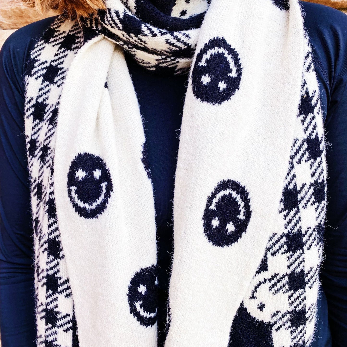 Cozy ivory scarf with black smiley face patterns and a classic checkered design, worn by a model on a navy top.