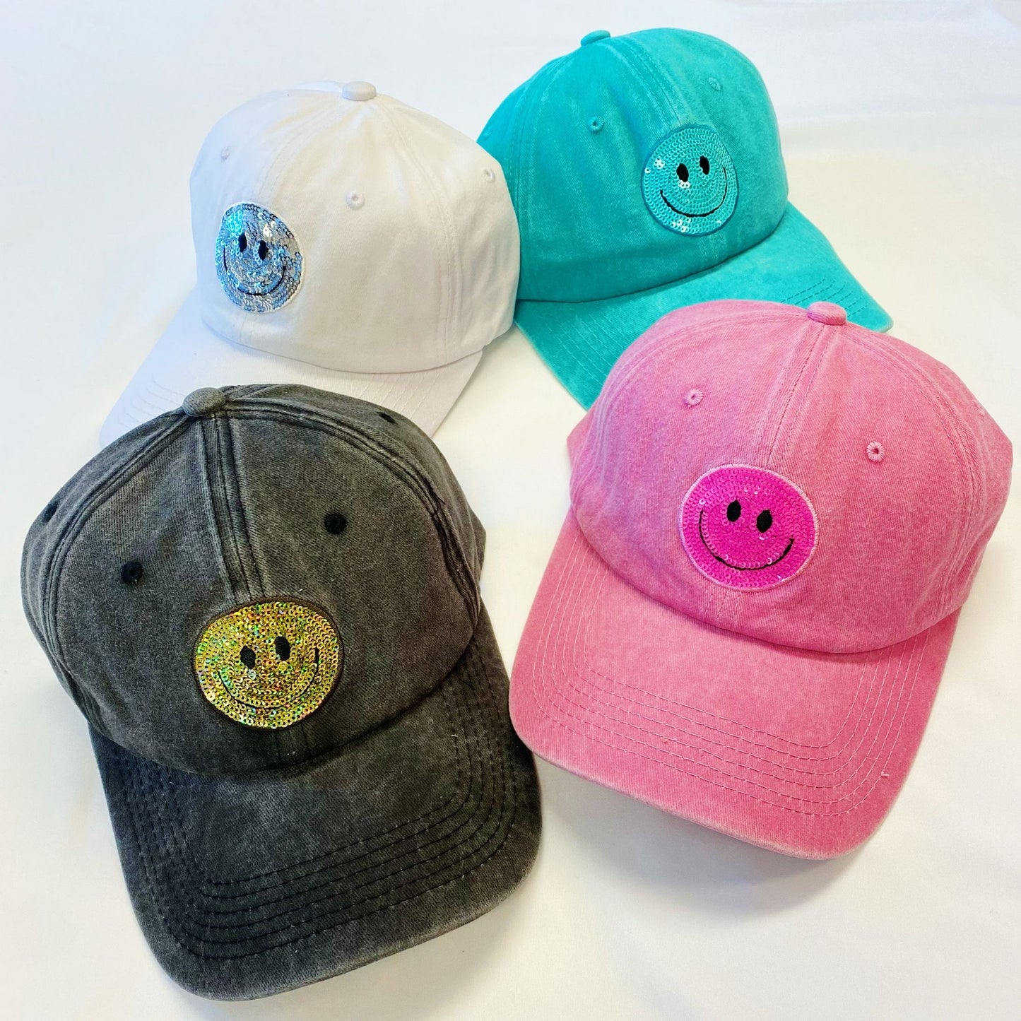 Colorful baseball caps with smiley face designs in white, teal, pink, and gray, featuring sparkling embellishments.
