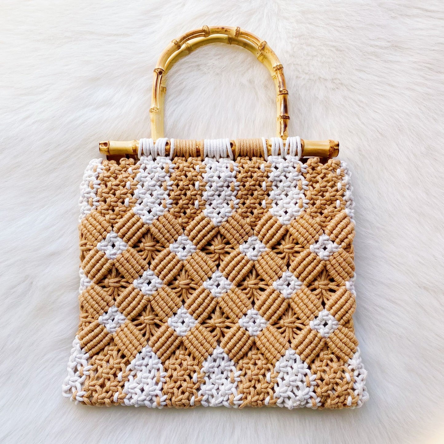 Handcrafted woven handbag with a stylish bamboo handle, featuring a beautiful geometric pattern in tan and white hues, resting on a fluffy white background.