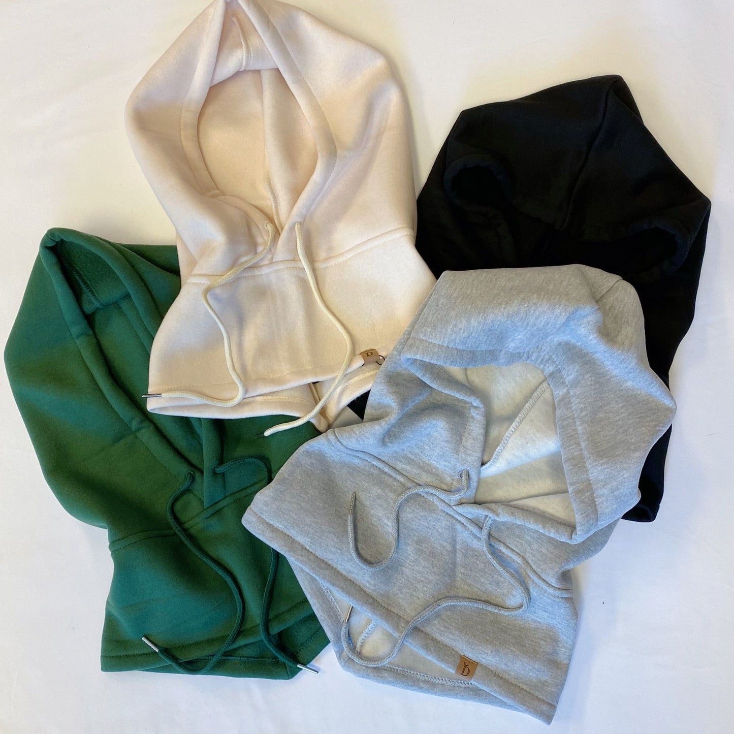 Four stylish hooded sweatshirts displayed in assorted colors: cream, black, gray, and green, featuring drawstrings and a soft fabric texture.