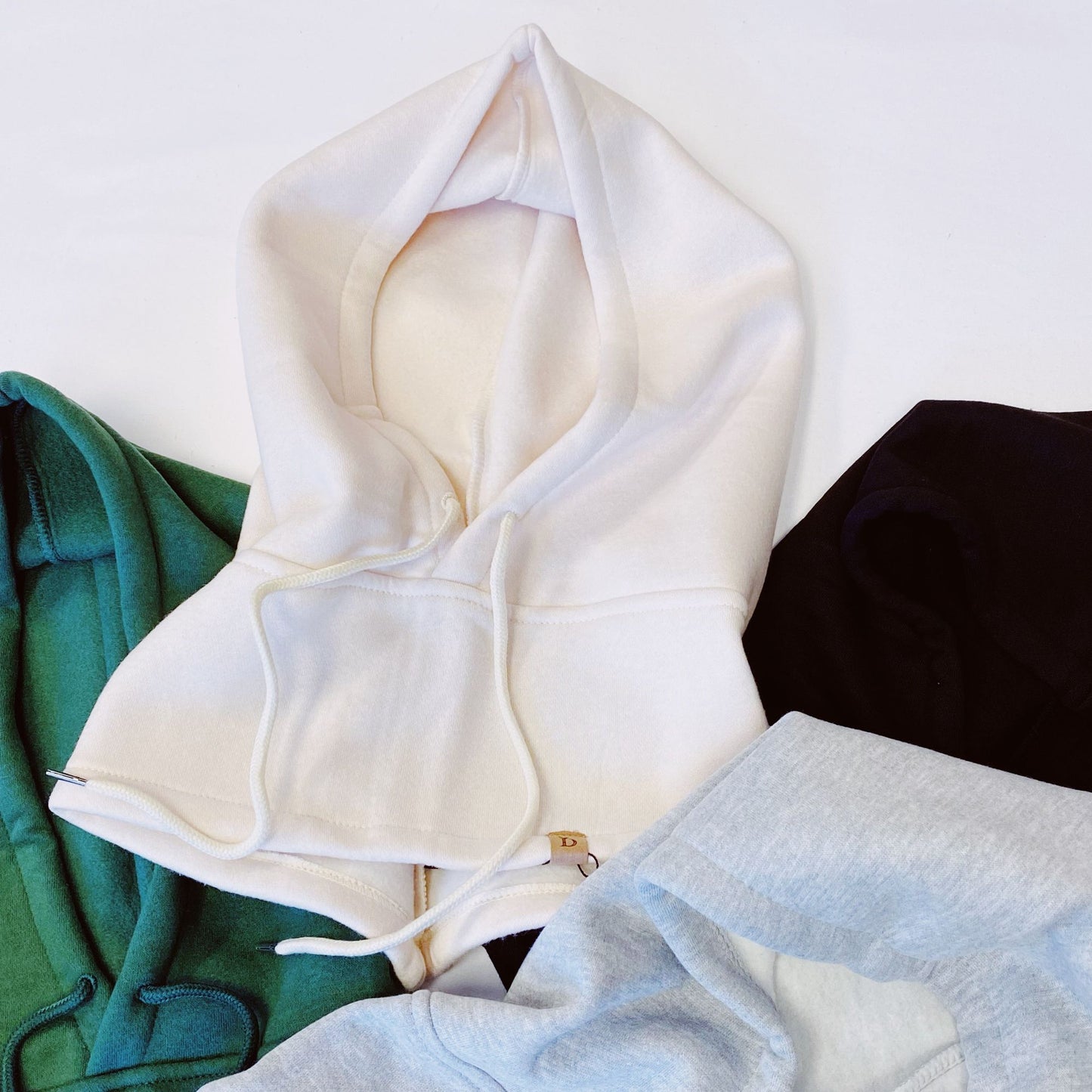 A collection of cozy hoodies in various colors including white, green, black, and gray, arranged on a white background, showcasing their soft fabric and adjustable drawstrings.