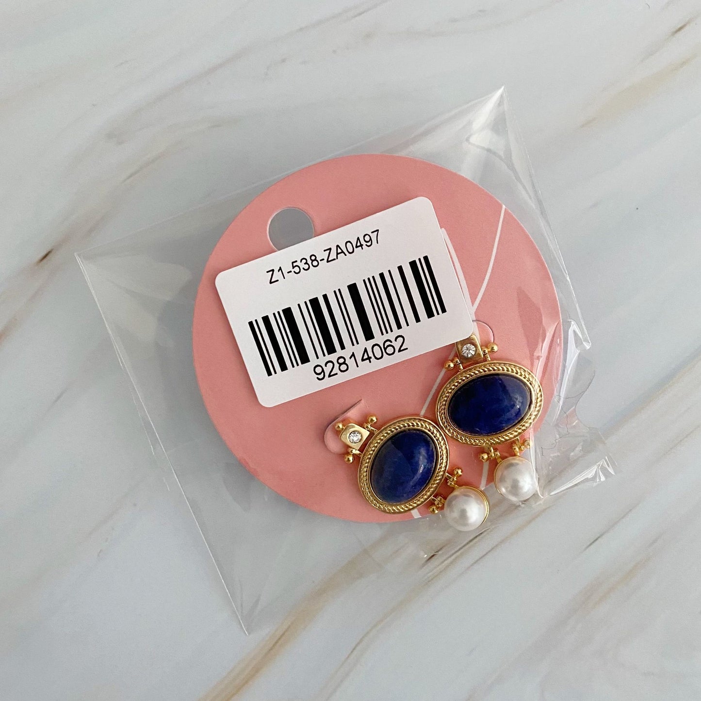 Gold and blue stone earrings with pearl accents in clear packaging on a pink backing