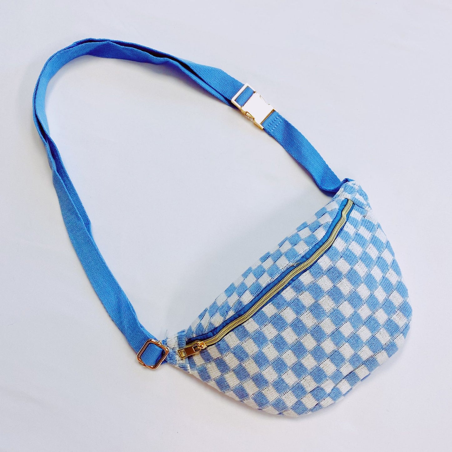 Blue and white checkered fanny pack with gold zipper and adjustable blue strap, perfect for stylish and convenient accessory storage.