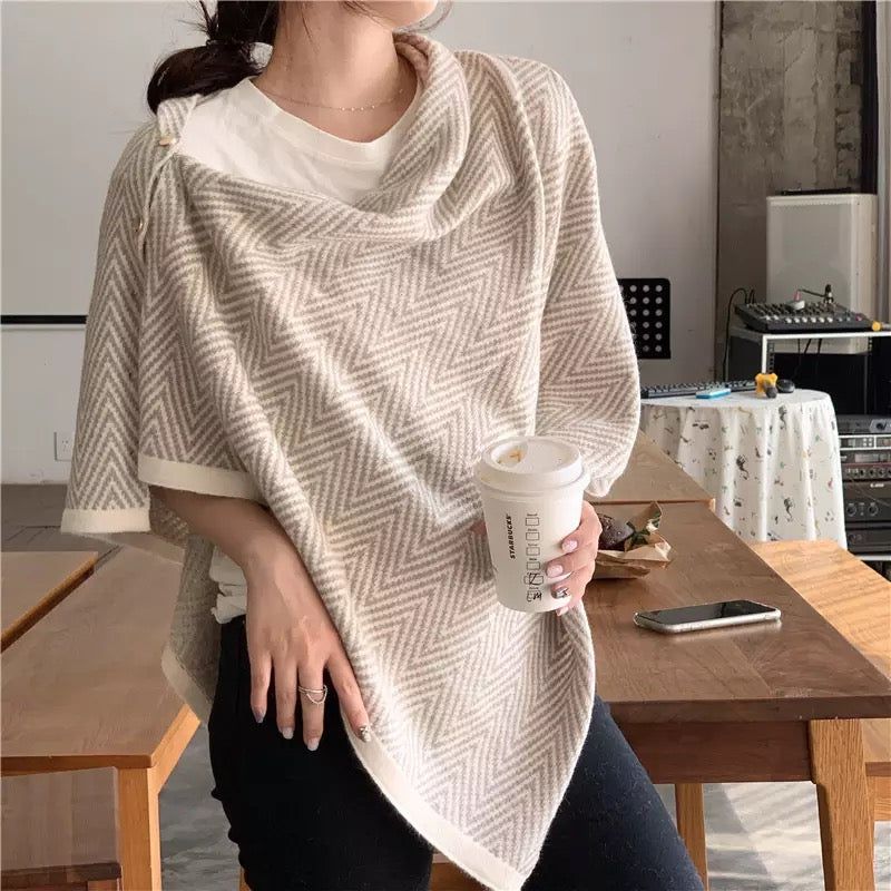 Casual woman in a stylish herringbone-patterned poncho, holding a coffee cup, showcasing a cozy outfit in a modern indoor setting.