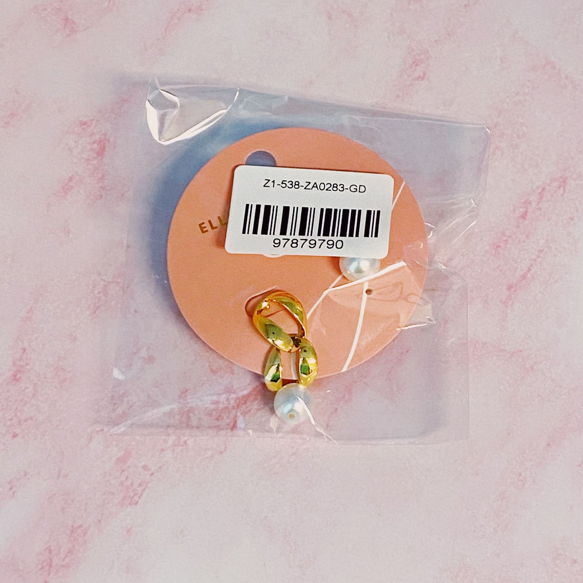 Gold and pearl drop earrings packaged on a peach-colored card, featuring a barcode and plastic wrapping.