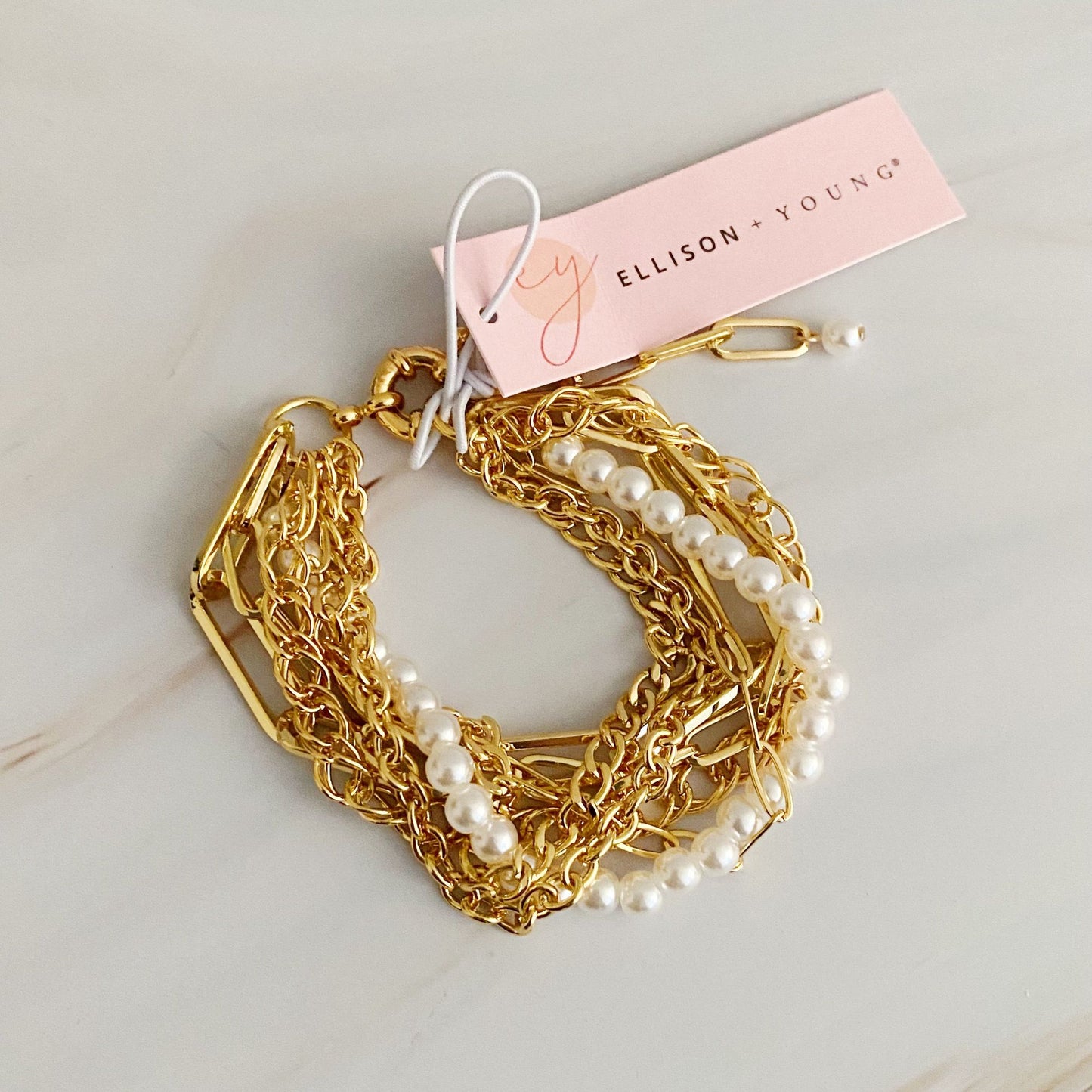 Gold layered bracelet with pearls, featuring a tag from Ellison + Young, displayed on a light marble background.