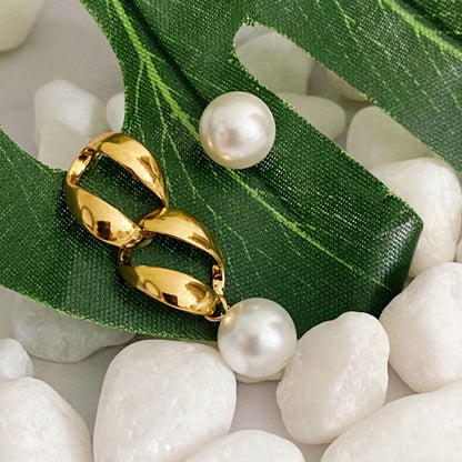 Gold hoop earrings with pearl drops resting on a green leaf atop white decorative stones, showcasing elegant jewelry design.