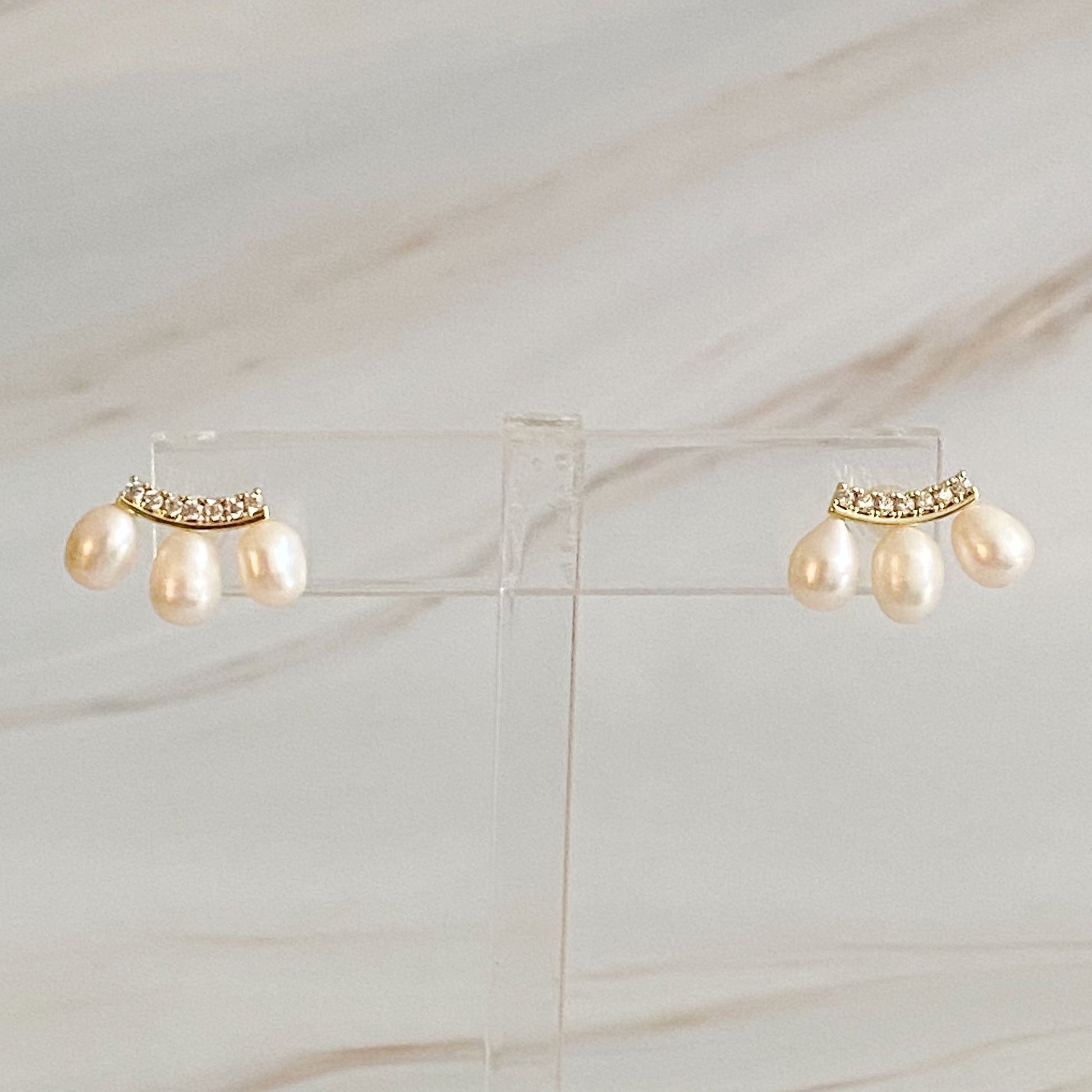 Elegant pearl drop earrings with sparkling crystal accents, set against a light marble background.