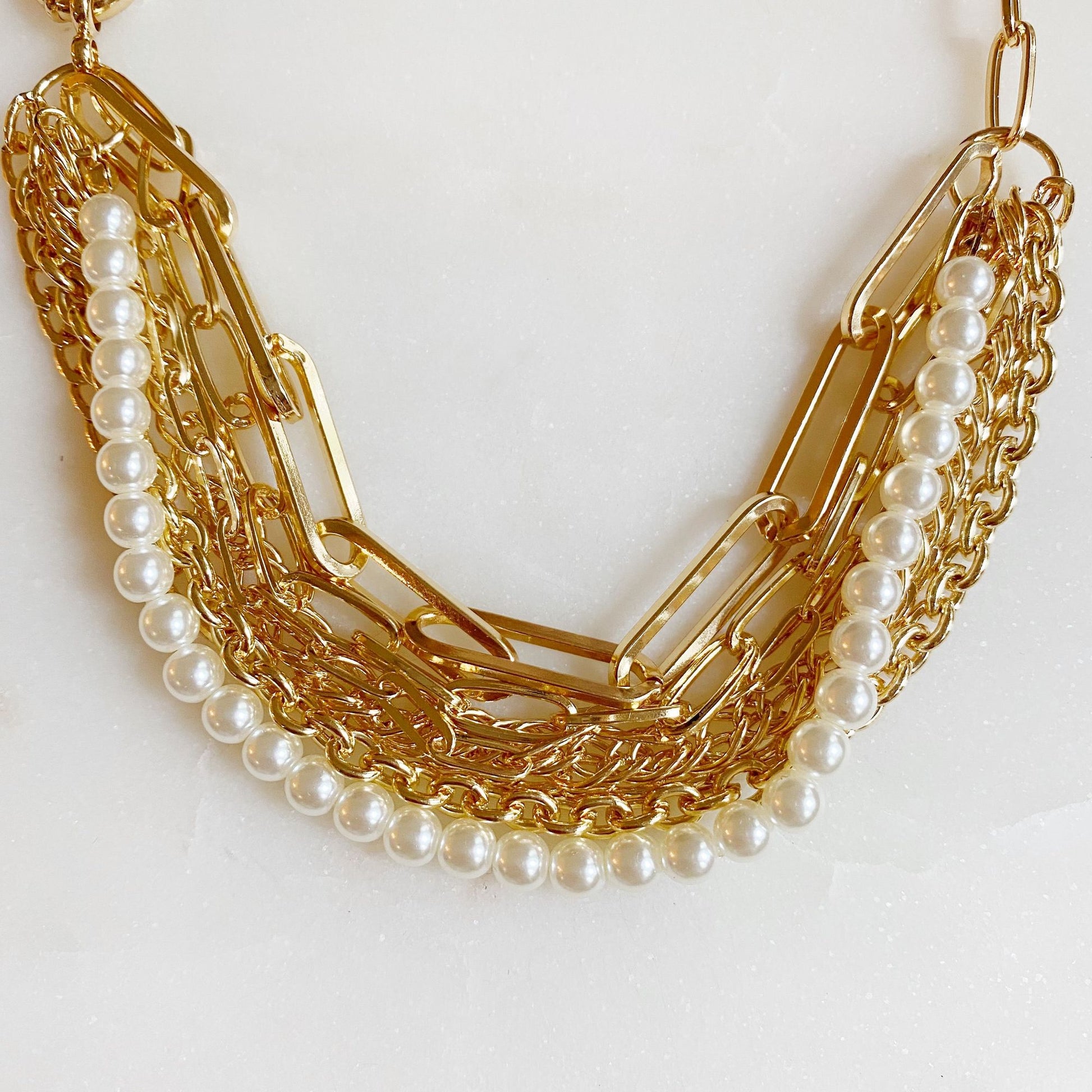 Gold chain necklace featuring layered strands of shiny gold links and elegant pearl accents on a light background.