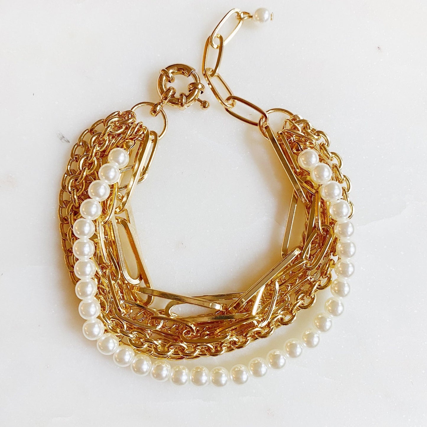 Gold chain bracelet with pearl accents on a marble background