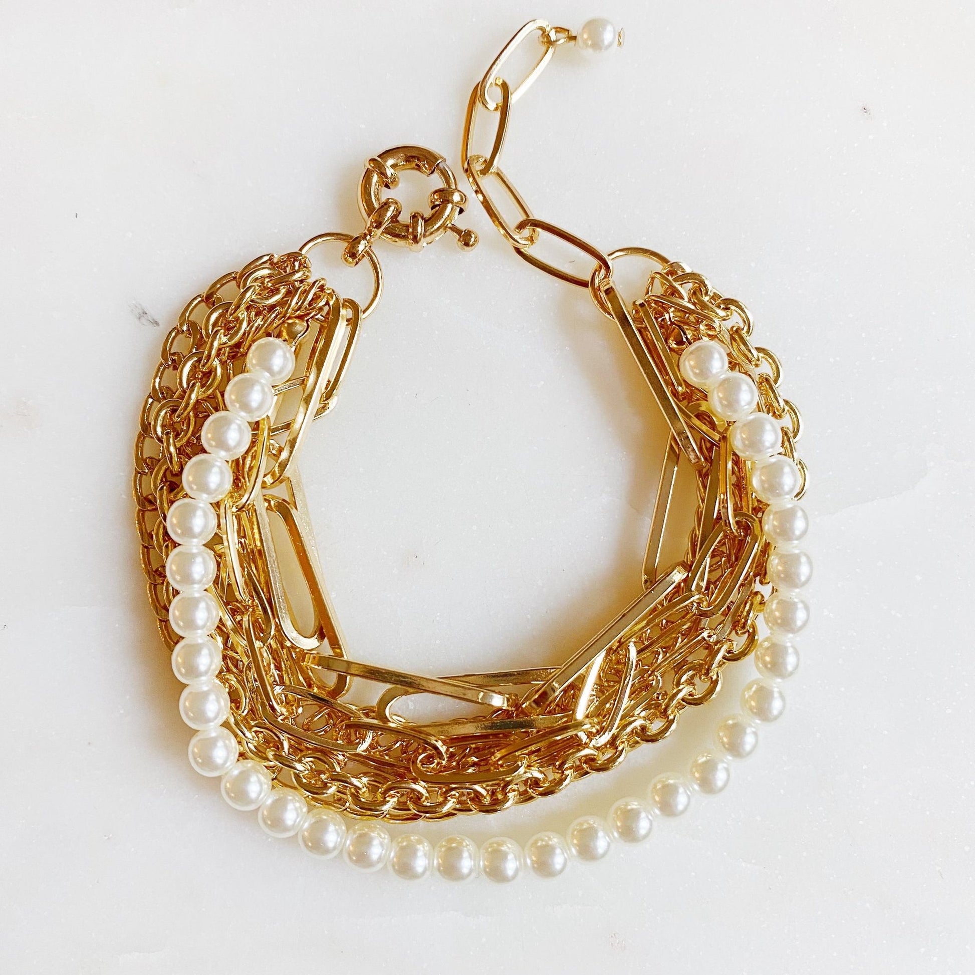 Gold chain bracelet with pearl accents on a marble background