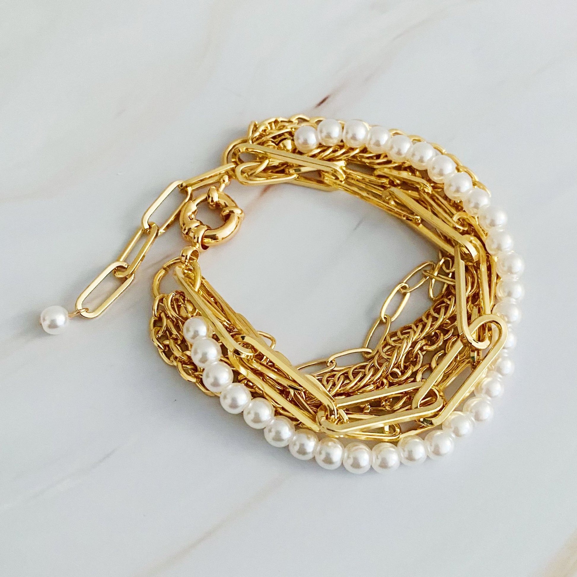 Elegant gold chain bracelet interspersed with luminous freshwater pearls, featuring a stylish clasp and layered design, set against a light marble background.