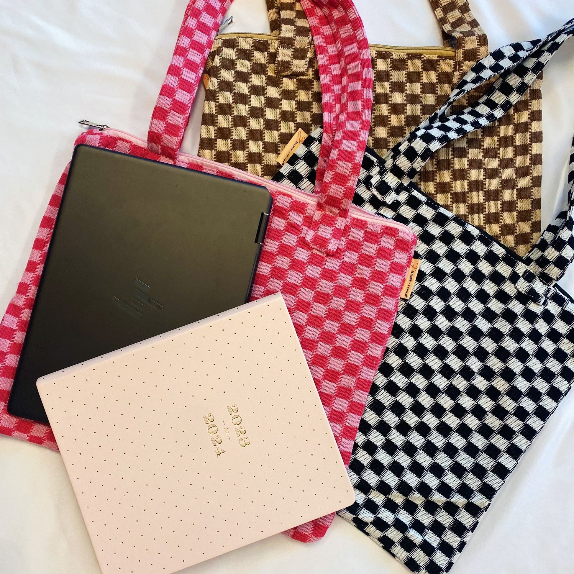 Colorful checkered tote bags in pink, brown, and black with a laptop and a planner, showcasing stylish organization for school or work essentials.