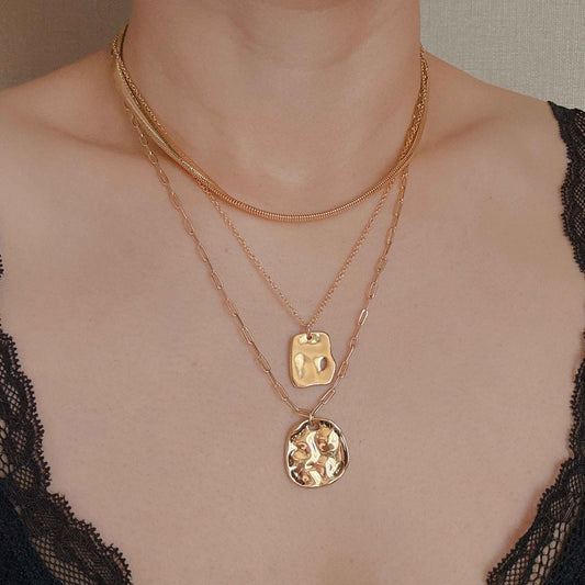 Layered gold necklaces featuring delicate chains and unique pendants, styled on a model wearing a lace top.