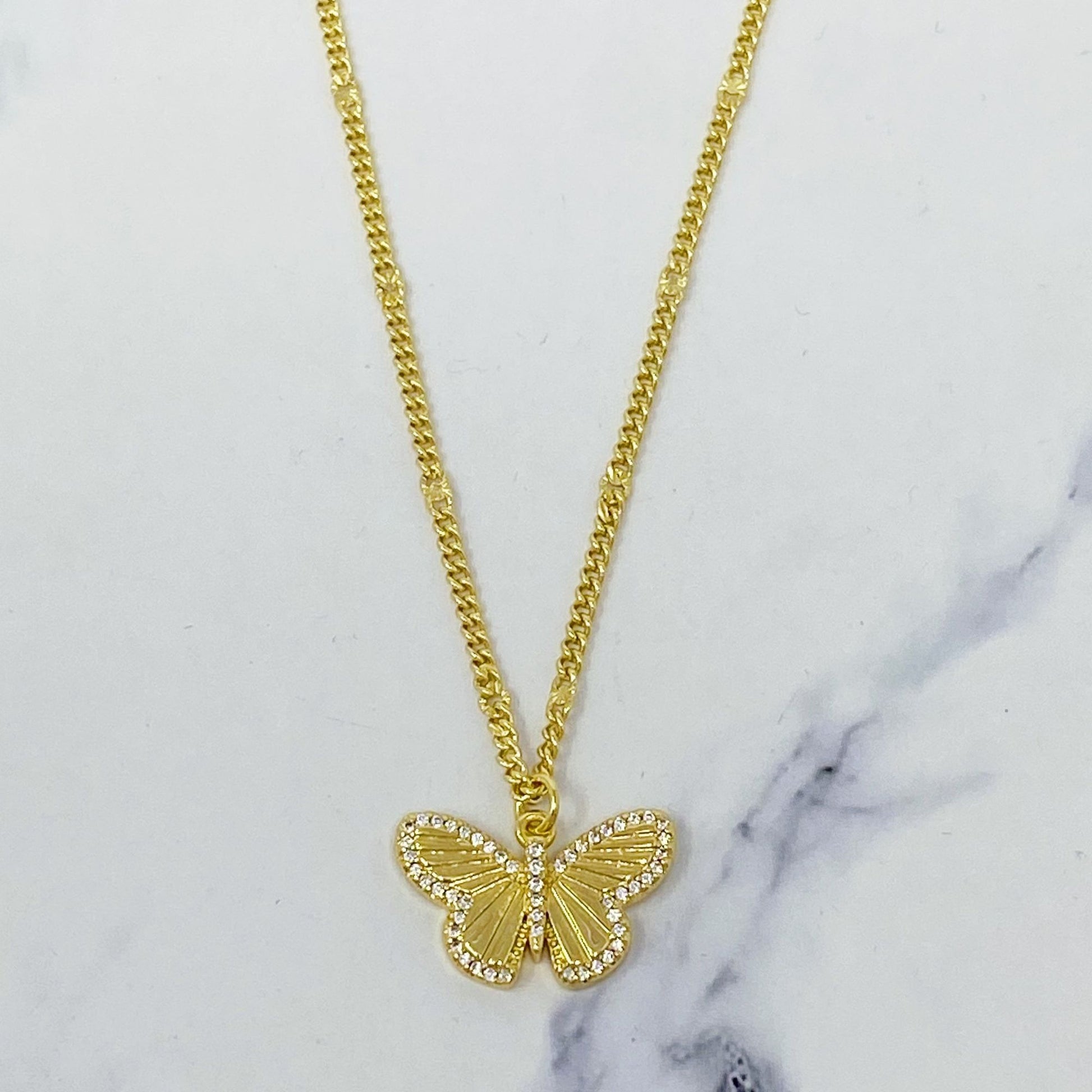 Gold butterfly pendant necklace with sparkling rhinestones on a delicate chain against a marble background.