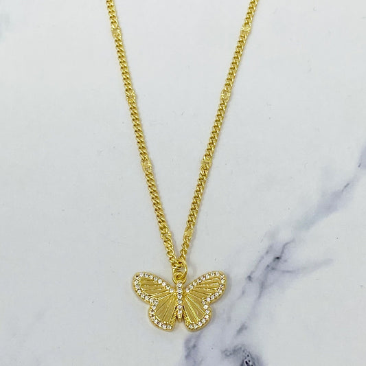 Gold butterfly pendant necklace with sparkling rhinestones on a delicate chain against a marble background.