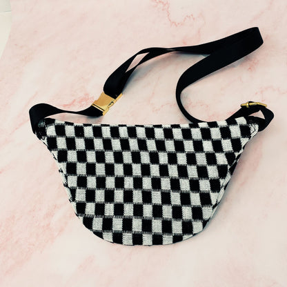 Black and white checkered fanny pack with adjustable black strap and gold buckle, placed on a pink marble background.