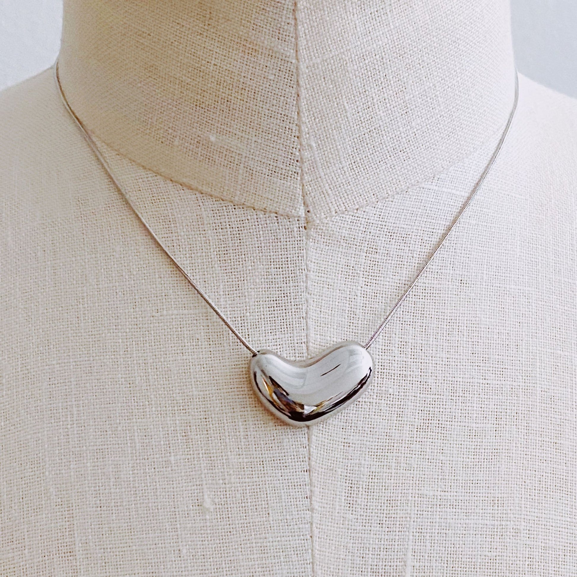 Stylish polished silver heart-shaped pendant necklace displayed on a linen mannequin, featuring a delicate silver chain, perfect for elegant occasions or everyday wear.