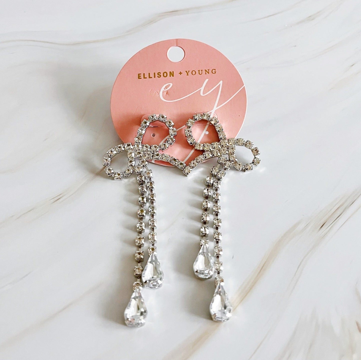 Elegant rhinestone bow hair clips with dangling crystal accents on a pink branded card by Ellison + Young.